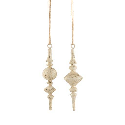 A pair of distressed, vintage-style hanging bead ornaments in a warm cream or off-white color with brown speckling, suspended by thin twine against a plain white background.