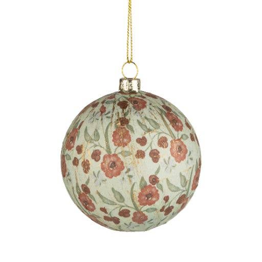 A round hanging Christmas ornament with a distressed off-white background and a vintage-style floral pattern in muted red and green, suspended by a gold string.