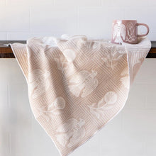 A beige and white patterned kitchen towel draped over a dark wooden counter, with a matching pink ceramic mug resting on the counter against a white tiled wall.