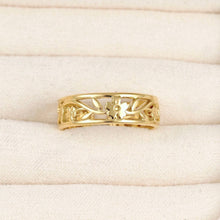 A gold ring with an openwork floral filigree design, displayed on a textured cream-colored fabric surface.