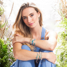 Woman wearing multiple bracelets and a necklace with a natural background