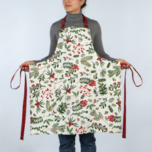 Person wearing a festive apron with holly and berry pattern on a plain background