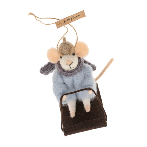 Decorative mouse ornament with a hat and scarf, sitting on a snow sled, on a white background.