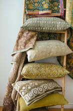 Stack of patterned pillows on a wooden ladder against a white wall.