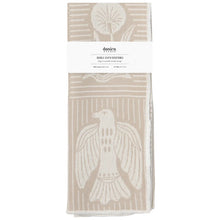 A folded double-cloth dishtowel by Danica, featuring a cream-colored bird and geometric patterns on a warm beige background, wrapped with a white paper label.