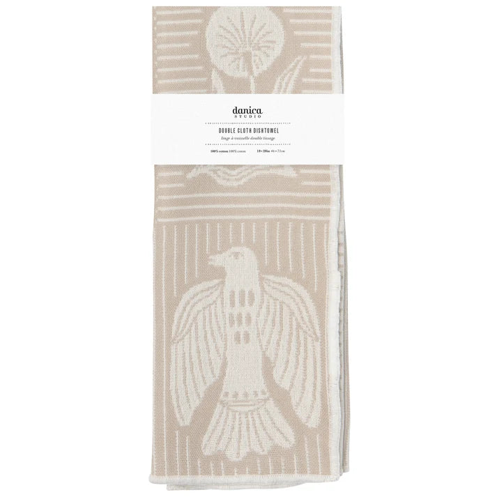 A folded double-cloth dishtowel by Danica, featuring a cream-colored bird and geometric patterns on a warm beige background, wrapped with a white paper label.