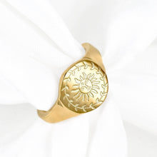 A gold signet ring featuring an engraved sun and leafy wreath design, displayed on a white fabric napkin.