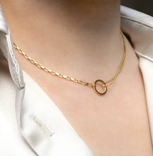 Gold necklace with a small ring pendant on a person wearing a white shirt.