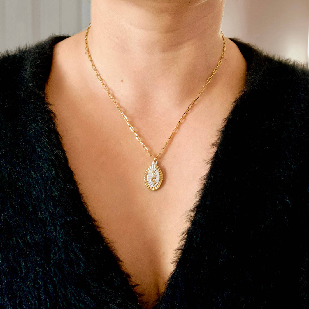 A close-up of a person wearing a delicate gold chain necklace with an oval pendant featuring a sunburst pattern of small clear stones.