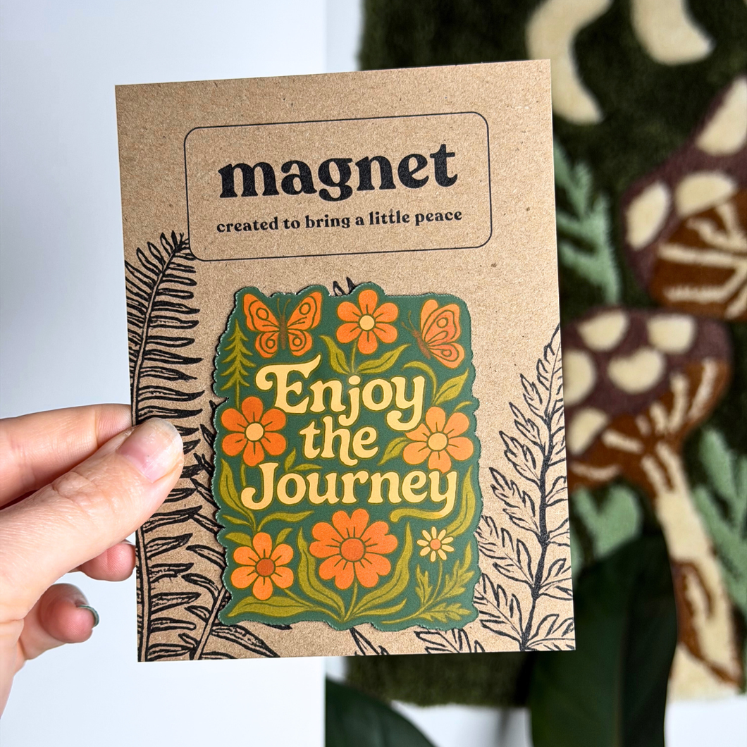 Cardboard magnet with floral design and text 'Enjoy the Journey' held by a hand.