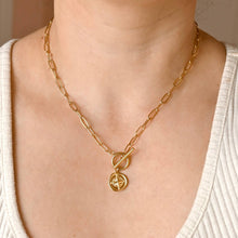 Gold chain necklace with a pendant on a person wearing a white top.