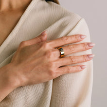 Hand wearing a gold ring with a diamond on a beige fabric background