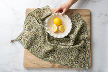 Floral print tea towel draped over a wooden cutting board with lemons on a white marble surface