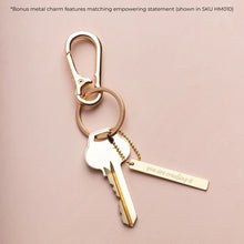 Gold key-shaped keychain with a tag on a pink background