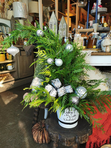 Decorative Christmas arrangement with greenery and silver ornaments on a wooden surface.