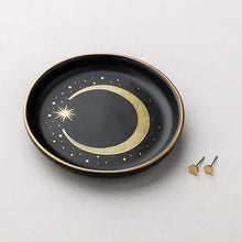 Black trinket tray with gold crescent moon design on a light gray background with a pair of earrings