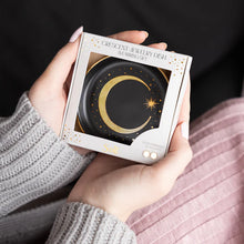 Person holding a box of a crescent jewelry dish with a black and gold design.