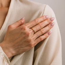 Hand wearing a gold ring on beige fabric