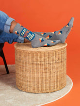 Person wearing patterned socks with text and triangles, sitting on a woven stool against an orange wall.