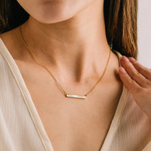 Gold necklace being worn by a person with a neutral background