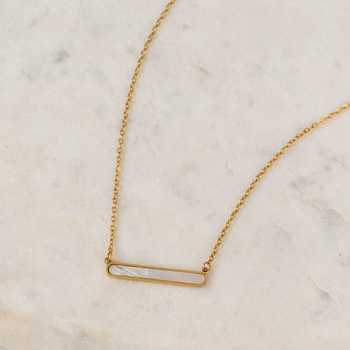 Gold necklace with a shell inlay bar pendant on a marble surface