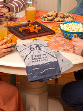 People around a table with snacks and a board game, featuring a towel with text.