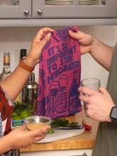 Two people in a kitchen with a colorful towel and glass of water.