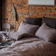Bed with mauve colored bedding against a brick wall