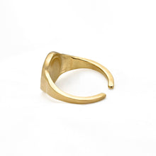 A gold-toned metal signet ring with a wide, chunky band and a flat, slightly tapered face, photographed on a clean white background.