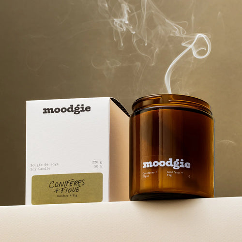 Brown candle with 'moodgie' branding and smoke rising, next to a white box with 'moodgie' branding.
