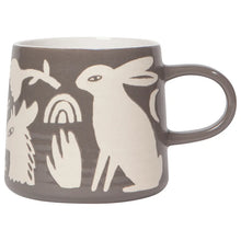 A ceramic mug with a dark gray exterior and cream-colored minimalist animal and nature illustrations, including a rabbit, bird, hand, and rainbow, shown on a plain white background.