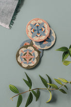 Set of four decorative coasters with floral patterns on a green surface with leaves.
