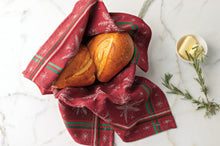 Two loaves of bread wrapped in a red cloth with green stripes on a white marble surface.