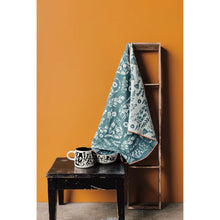 Teal patterned towel draped over a wooden ladder against an orange wall.