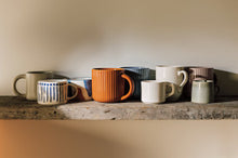 Set of colorful mugs on a wooden shelf against a neutral wall