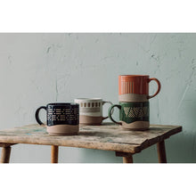 Four ceramic mugs on a wooden table against a textured wall.