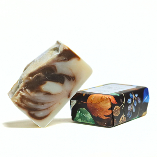 A handmade rectangular bar of soap with brown and cream swirls, shown standing next to its decorated dark-colored paper packaging box on a white background.