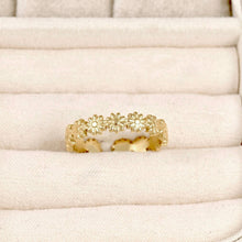 A gold ring featuring a continuous pattern of small daisy-like flowers, displayed on a cream-colored textured ring box.