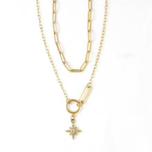 A gold layered necklace featuring a paperclip chain, a link chain, a ring connector, and a small starburst pendant with a clear central stone, shown on a white background.
