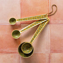 Set of gold and green patterned measuring spoons on a tiled surface