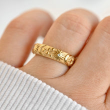 Gold ring with intricate design on a finger against a white background